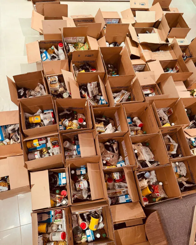 Decenas de cajas de cartón abiertas y llenas de alimentos, preparadas en el suelo antes de una entrega.