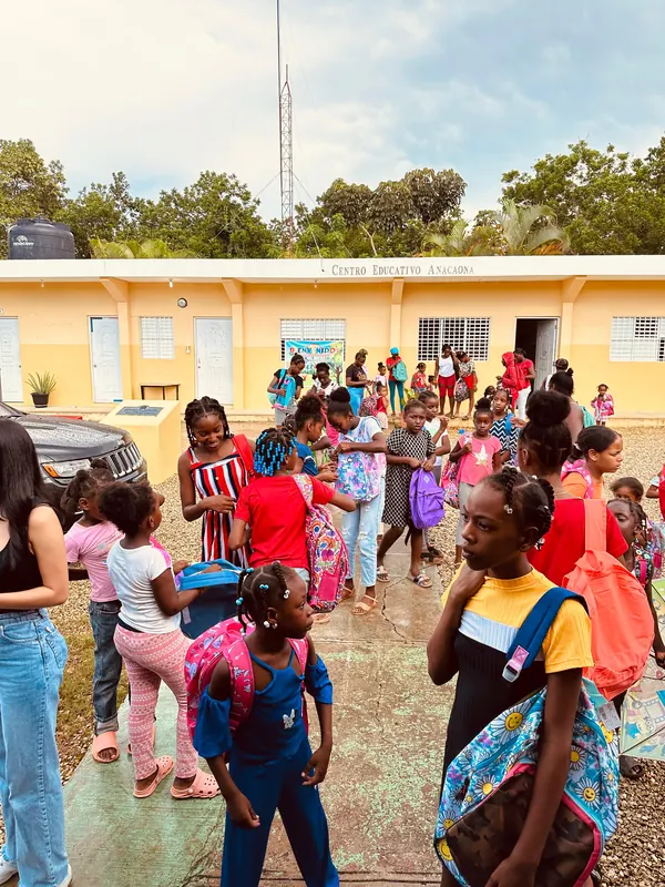 Decenas de niñas y niños con sus mochilas nuevas puestas, reunidos en el patio de un centro educativo.