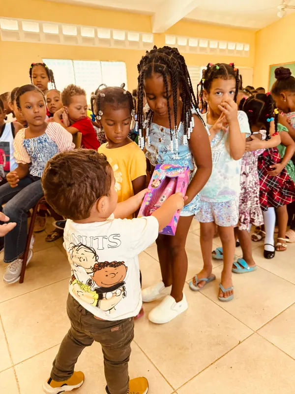 Niñas y niños esperan su turno dentro de un aula mientras se reparten los regalos, uno por uno.