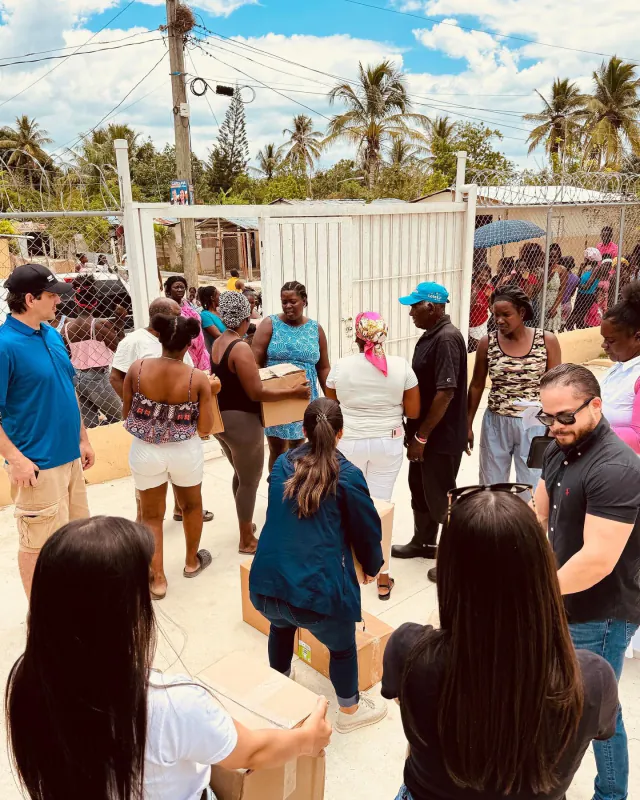 Voluntarios y vecinos, con cajas en las manos, durante una distribución de alimentos a la entrada de una comunidad.