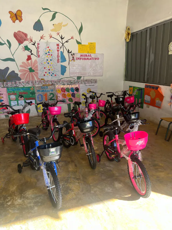 Bicicletas nuevas con canastas de colores, ordenadas dentro del aula de un nivel inicial.