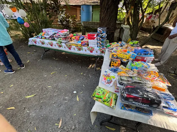 Una mesa larga al aire libre, cubierta de juguetes ordenados, preparada antes de comenzar la entrega.