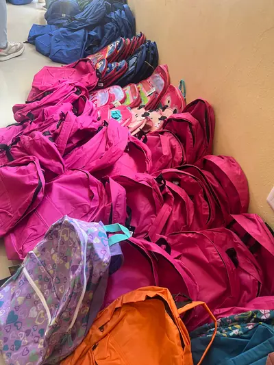 Una pila de mochilas rosadas y de colores, apoyadas contra la pared antes de una entrega escolar.