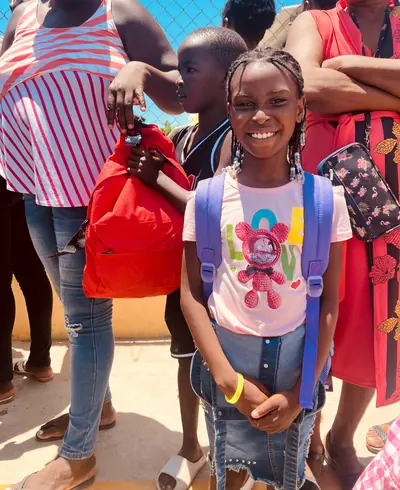 Una niña sonríe con su mochila morada nueva puesta, en medio de una entrega de útiles escolares.