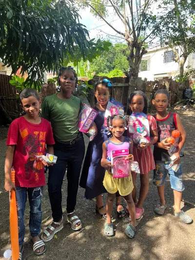 Un grupo de niños y niñas posa bajo un árbol mostrando los juguetes que acaban de recibir.