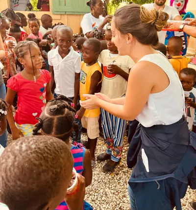 Una voluntaria reparte meriendas rodeada de niños y niñas que la esperan sonrientes en el patio de una escuela.