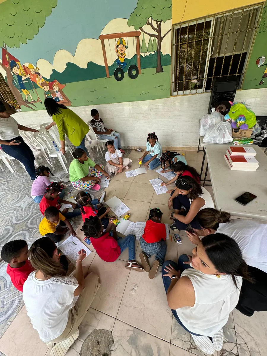 Vista desde arriba de un grupo de niños sentados en círculo en el piso de un aula, trabajando con voluntarias.