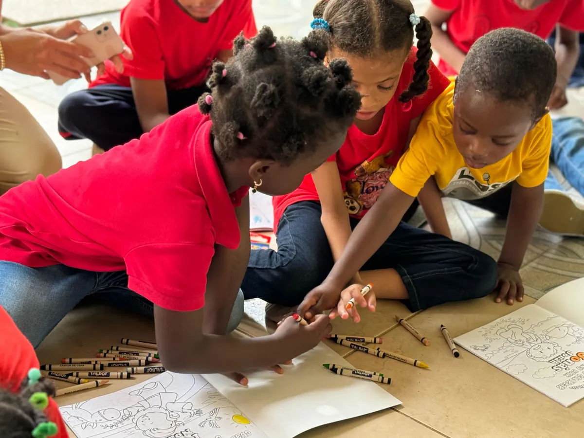 Dos niños comparten crayones y colorean sobre el piso, acompañados por una voluntaria, en una jornada de la fundación.